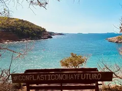 Banco de madera con el cartel #ConPlasticoNoHayFuturo frente a una cala de aguas turquesas