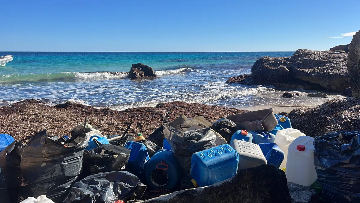 Garrafas y bidones de plástico recogidos en una cala rocosa de Formentera, con la lancha al fondo